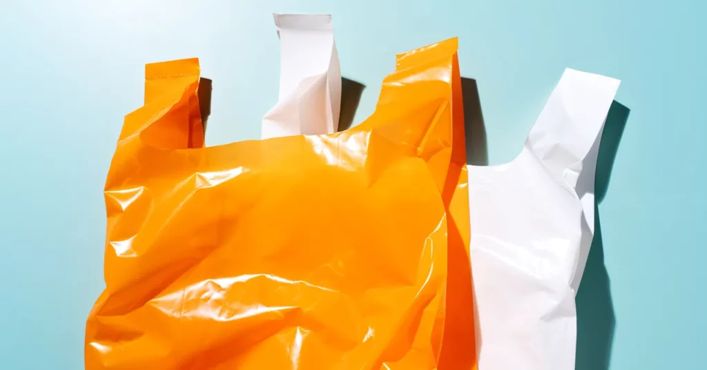 Kantong plastik berwarna oranye dan kantong plastik putih tumpang tindih pada tampilan dekat latar belakang biru.